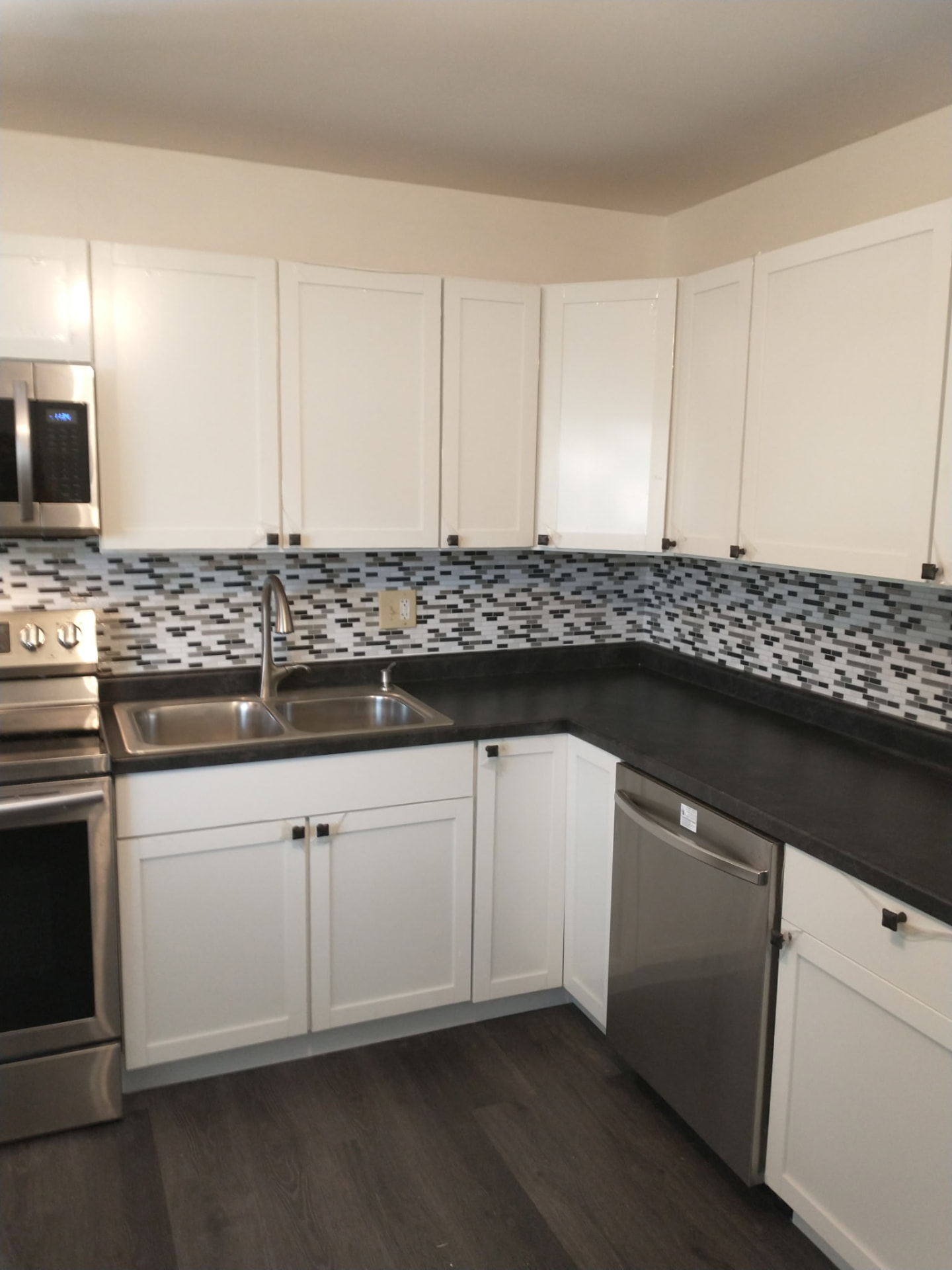 Remodeled kitchen with white cabinets, tile backsplash, and new laminate flooring